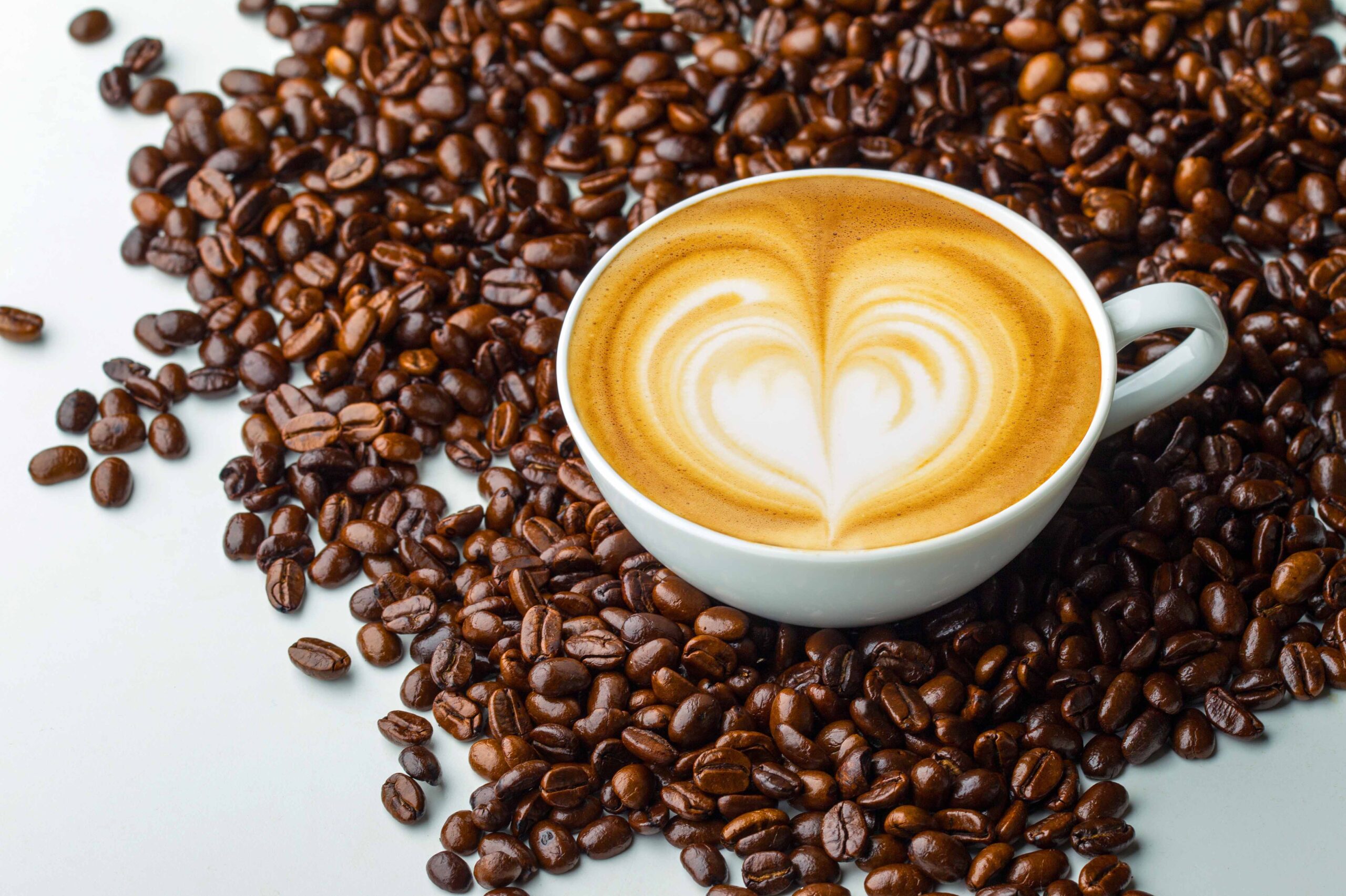 white coffee mug with heart latte surrounded by freshly roasted coffee beans