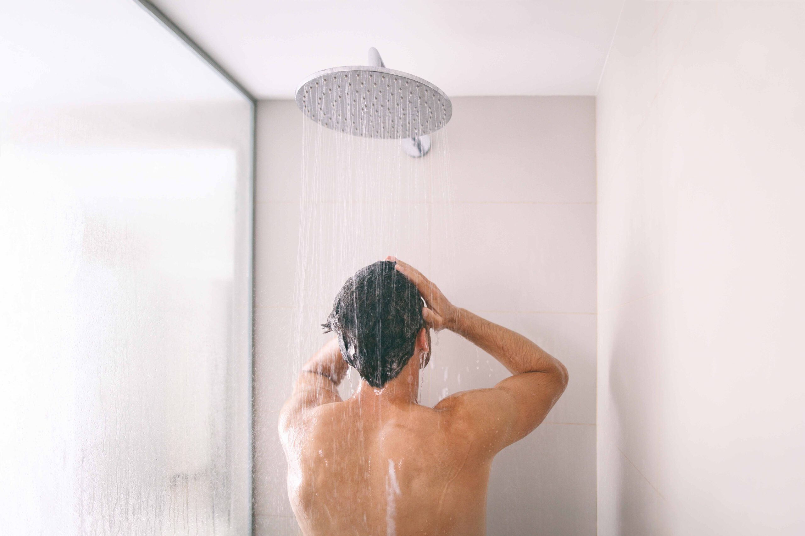 man rinsing hair in overhead shower